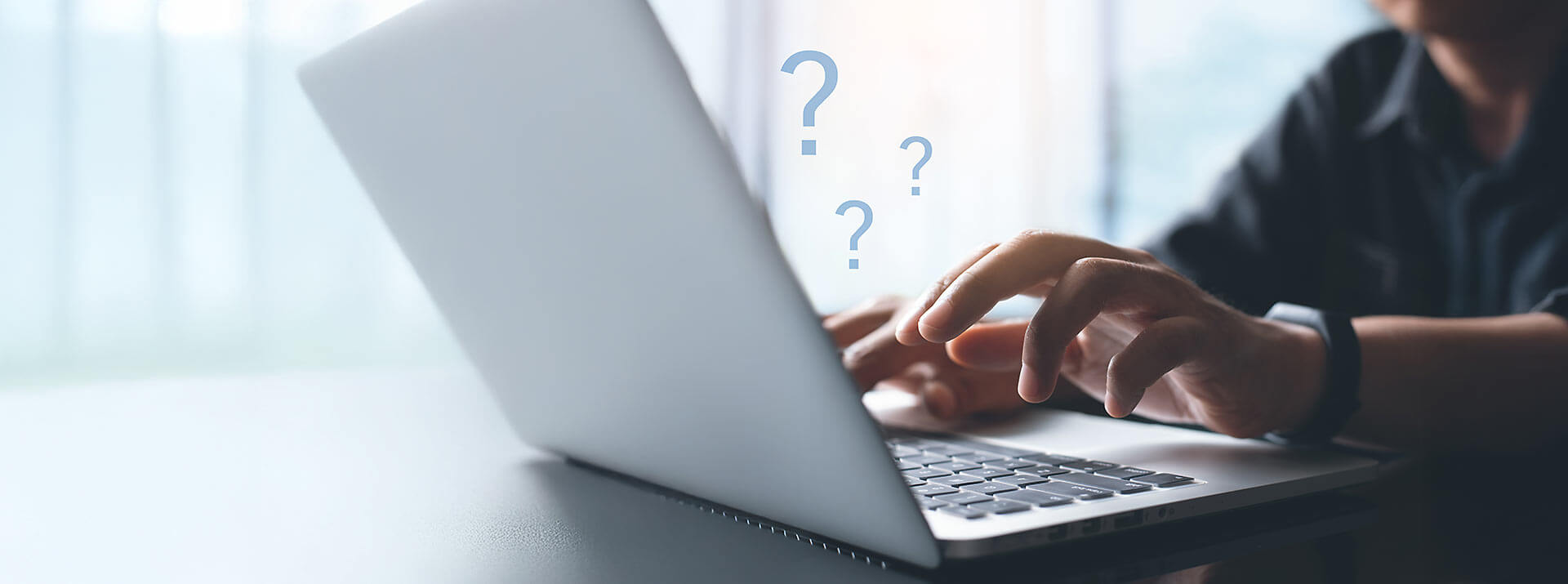 Laptop in Seitenansicht und Person die davor sitzt und etwas eintippt, drei blaue Fragezeichen über die Händen